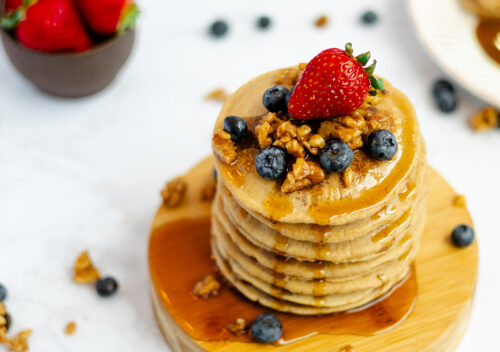 Naturally sweetened vegan pancakes fresh from the skillet, folded and stacked, with a drizzle of vegan buttermilk syrup.