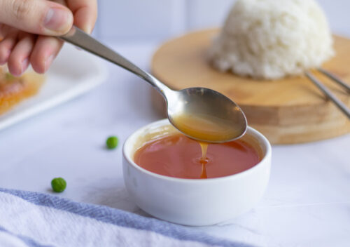 A small bowl of glossy sweet and sour sauce next to a plate of rice, shot from above.