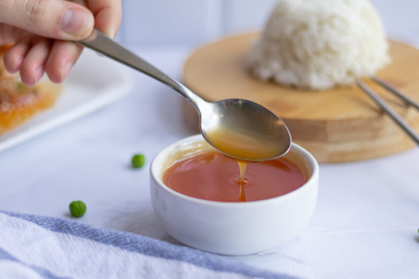 A small bowl of glossy sweet and sour sauce next to a plate of rice, shot from above.