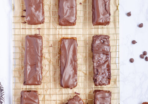 Close-up of homemade plant-based Twix bars made with layers of almond flour shortbread, date caramel, melted vegan chocolate on top, and some flaky sea salt.