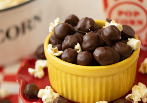 Bite-sized healthy cookie dough candies coated in chocolate surrounded by popcorn, ready to enjoy.