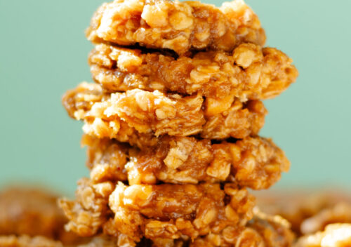 Chewy no bake peanut cashew cookies on parchment paper, topped with chopped peanuts, stacked on top of each other.