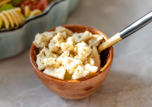 Close-up of vegan feta made from boiled tofu, crumbled over colorful pasta salad with tomatoes, cucumbers, and fresh herbs.