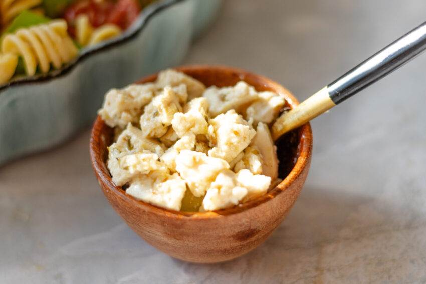 Close-up of vegan feta made from boiled tofu, crumbled over colorful pasta salad with tomatoes, cucumbers, and fresh herbs.