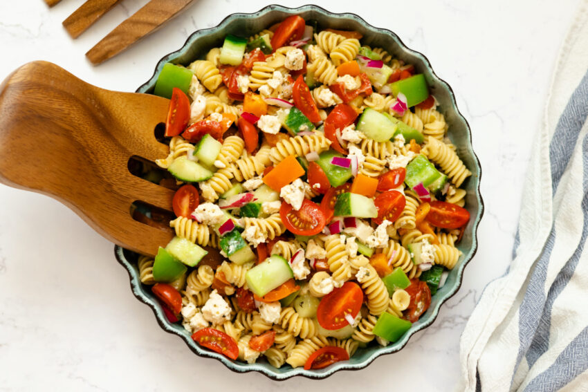 Bowl of colorful vegan pasta salad with avocado dressing, topped with vegan feta