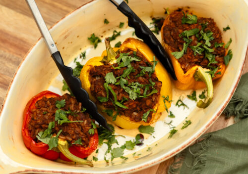 Overhead view of vegan stuffed bell peppers filled with hearty lentil sloppy joe mixture, baked until tender, and garnished with fresh parsley in a white baking dish.