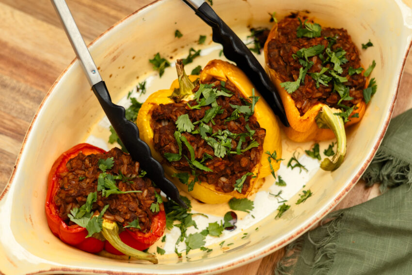Overhead view of vegan stuffed bell peppers filled with hearty lentil sloppy joe mixture, baked until tender, and garnished with fresh parsley in a white baking dish.