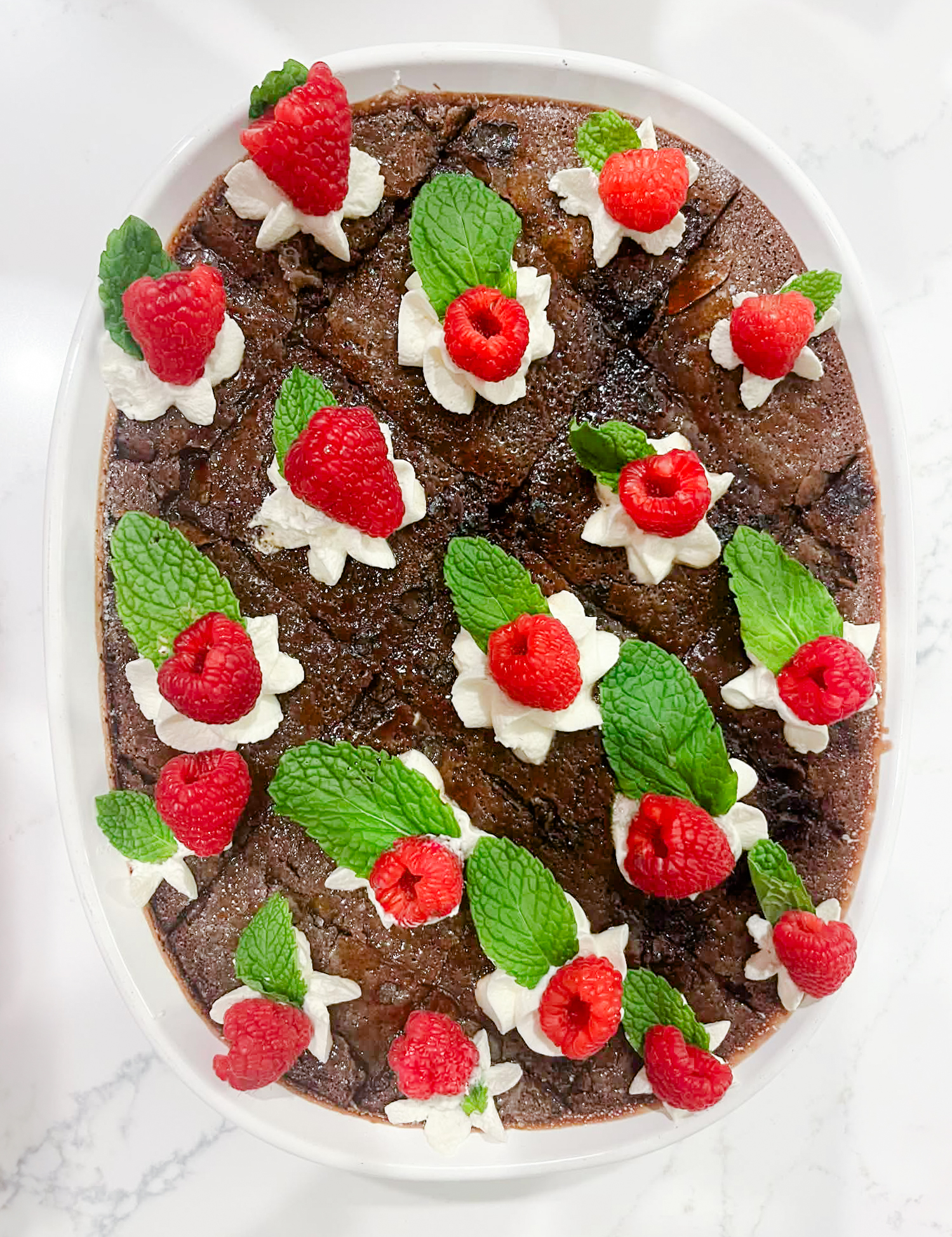 “Chocolate crème brûlée casserole with a caramelized sugar topping, piped whipped cream, fresh raspberries, and mint leaves.”